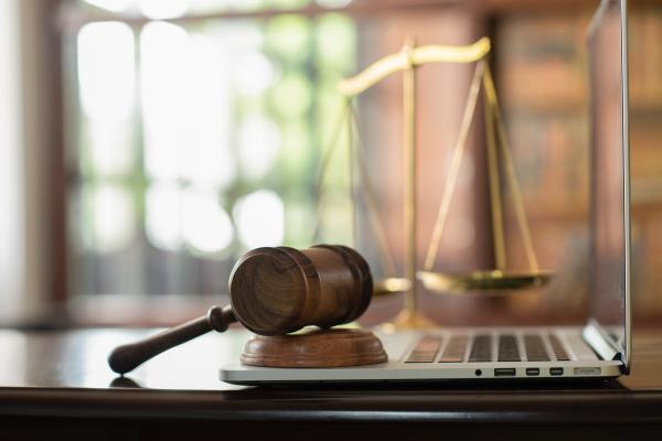 gavel sitting on a laptop with weights of justice in the background