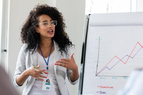 teacher with jacket, glasses and curly hair explains chart to adults