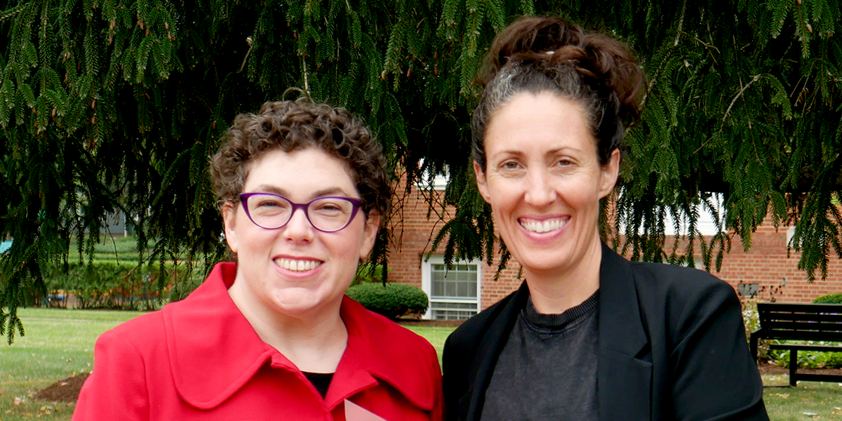 two people standing in front of trees smiling