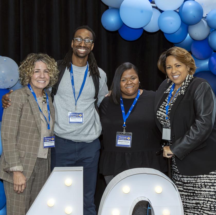 four people smiling and standing in front of blue balloons