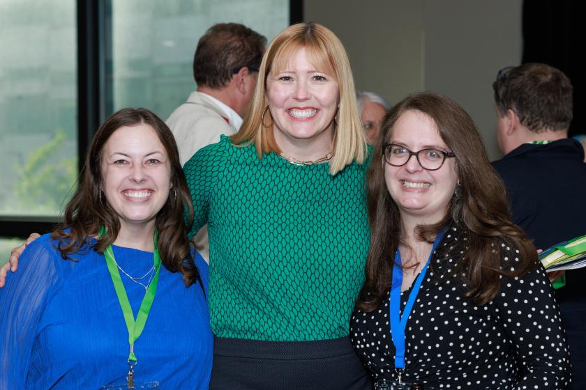 three people standing with arms around each other smiling 