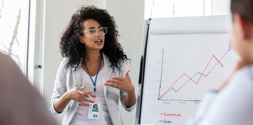 teacher with jacket, glasses and curly hair explains chart to adults